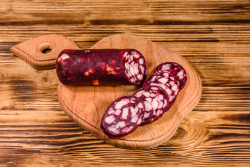 Cutting board with sliced salami sausage on a wooden table