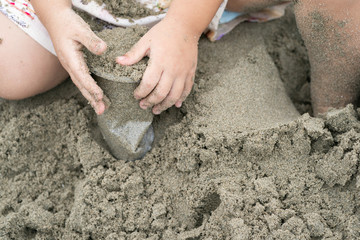 Kid holds and plays sand in the plastic cup on the beach.