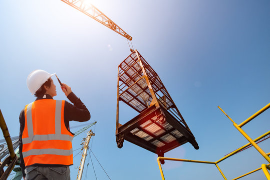stevedore or foreman, engineering, loading master talks to crane driver by walkie talkie for safety lifting  the goods shipment, lifting by gantry crane, working at risk on the high level insurance