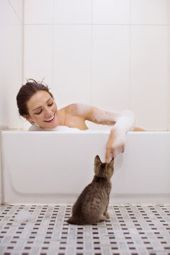 Young woman taking bath and playing with cat 