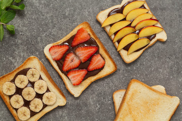 Delicious toast  bread with fresh strawberry, banana, peach and chocolate paste on grey background. Delicious breakfast. Top view