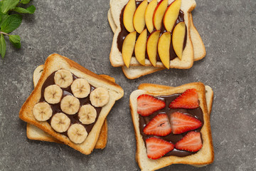Delicious toast  bread with fresh strawberry, banana, peach and chocolate paste on grey background....
