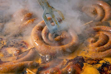 Hand Holding Barbecue Tongs With a Frying Sausage