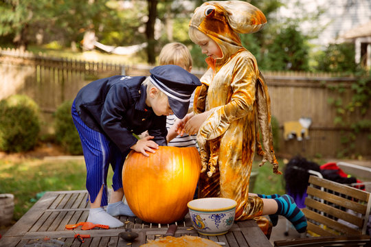 Boys (4-5, 6-7) wearing halloween costumes and reaching into Jack o' Lantern 