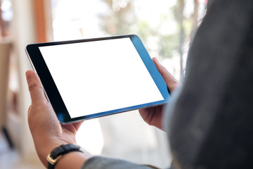 Mockup image of a woman holding black tablet pc with blank white screen while sitting in cafe
