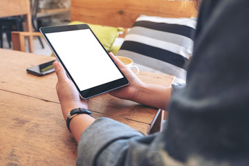 Mockup image of woman's hands holding black tablet pc with blank screen on wooden table in cafe