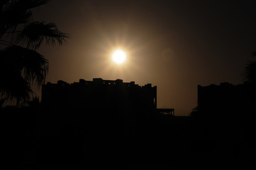 Silhouette of the building in the eastern style and palm trees on the background of the sun during...