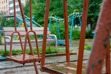 Fototapeta premium Old children's swing on the playground in the rain. Concept - sad childhood