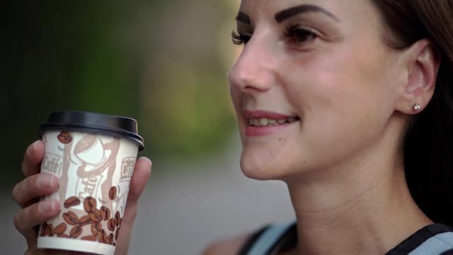 beautiful young Caucasian woman drinking takeaway coffee on the street. Beautiful girl on the street with coffee smiling and enjoying. close-up