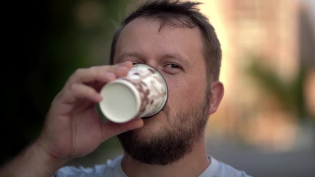 Bearded man drinking takeaway coffee on the street and smiling. close-up