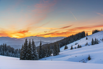 A colorful evening with a beautiful sunset and dusk in the snow-covered mountains of the mountains with mountain houses in the Ukrainian Carpathians overlooking Hoverla and Petros.