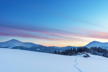 A colorful evening with a beautiful sunset and dusk in the snow-covered mountains of the mountains with mountain houses in the Ukrainian Carpathians overlooking Hoverla and Petros.