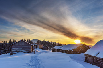 A colorful evening with a beautiful sunset and dusk in the snow-covered mountains of the mountains with mountain houses in the Ukrainian Carpathians overlooking Hoverla and Petros.