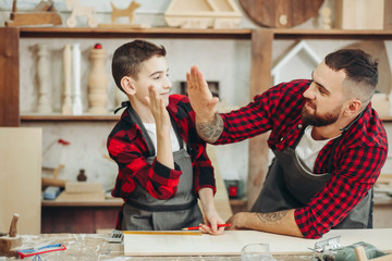 father and little son giving high five while visiting woodworking masterclass at workshop - obrazy, fototapety, plakaty