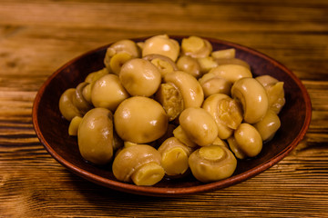Ceramic plate with canned mushrooms on wooden table