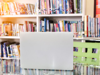 Laptop on glass table with bookshelf background.