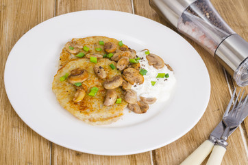 Rustic food concept. Fried potato pancakes with sauce and mushrooms on wooden table