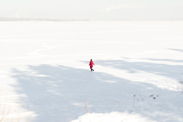 Naklejka na ściany i meble A girl in a red jacket walking on snow covered landscape in the winter. Top view.
