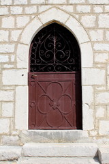 Venetian style metal entrance doors with strong hinges and polished door handle mounted on traditional stone wall with stone steps in front on warm sunny day