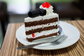 Black forest cake, fresh cream, cherry, and chocolate on top with a fork