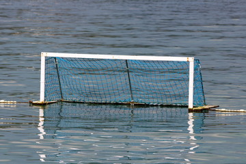 Water polo goal with white frame and blue net supported with rope and floating buoys resting on...