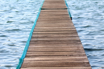 Wooden pier made of multiple narrow boards with nylon protection on edges over calm blue sea on...