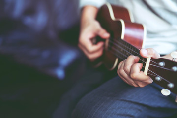Closeup of young man hands playing acoustic guitar ukulele at the sofa sit Enjoy living room.  