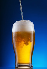 Light beer pouring into glass on blue background