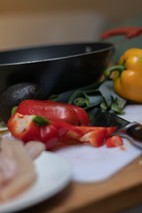 Chopped bell pepper surrounded by ingredients with wok as a backdrop and a knife next to it