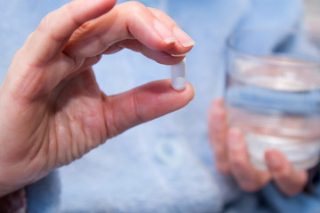 Woman with pills or capsules on hand and a glass of water