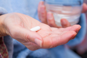 Woman with pills or capsules on hand and a glass of water