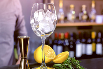 Barman puts ice on the wineglass for cocktail with lemon and rosemary. Hands close-up.