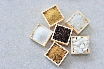 Roasted coffee beans and wooden box of brown sugar, raw sugar, cube sugar, rock sugar and white granulation sugar arround . sucrose or table sugar are the nutritive sweeteners.