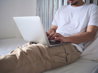 Cropped image of young Asian man typing on computer laptop on the bed. Internet of things concept.