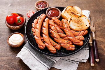 Grilled sausages and different sauce on a dark wooden background.