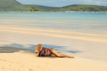 Woman with hat in purple bikini relaxing on tropical sandy beach in Las Galeras - Dominican Republic