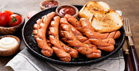 Grilled sausages and different sauce on a dark wooden background.