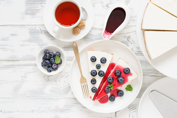 Cheesecake with fresh blueberry and berry sauce on white wooden table.