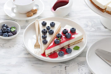 Cheesecake with fresh blueberry and berry sauce on white wooden table.