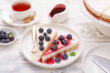 Cheesecake with fresh blueberry and berry sauce on white wooden table.