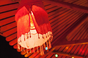Red homemade lampshade with a fringe of fabric against the background of a canopy of planks