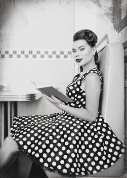 Retro (vintage) portrait of cute young woman sitting in cafe with book. Pin up style portrait of young woman in dress, black and white, texture effect