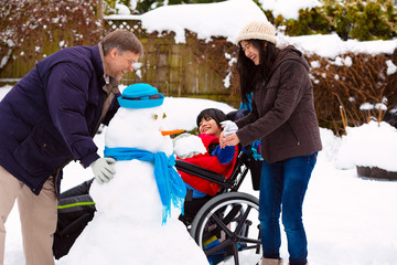 Disabled boy in wheelchair building snowman with family during  winter