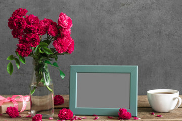 blank photo frame and rose flowers with cup of tea and gift box on rustic wooden table. mock up. still life