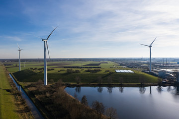 Wind turbines generating eco friendly green energy for a better environment on fields next to a canal near Waalwijk, Noord-Brabant, Netherlands.