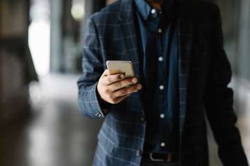 Hands of unrecognisable businessman walking and typing on his cell phone.