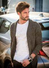 Portrait of young attractive man in white shirt leaning on his new stylish polished car outdoor in...
