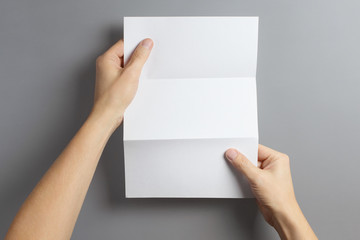 Hands holding a folded sheet of white paper on gray background