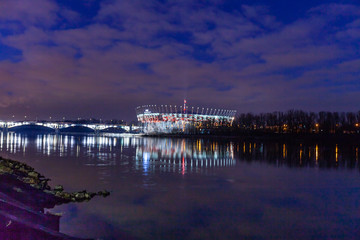 Naklejka premium WARSAW, POLAND - FEBRUARY 14, 2019:Night illuminated skyline view with water reflections, National Stadium in Warsaw.