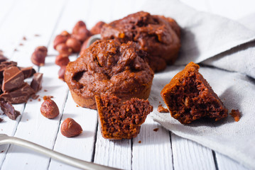 broken chocolate muffin and hazelnuts, fork on white wood table